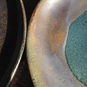 May include: Two ceramic plates with a speckled glaze in shades of brown, green, and gold. The plates have a slightly uneven, handmade look.