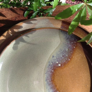 May include: A stack of ceramic plates with a unique color gradient. The plates transition from a light green to a warm brown hue, with a speckled texture. The rims are a darker brown. Green leaves are in the background.