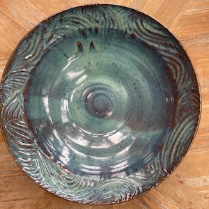 May include: A large, round ceramic bowl with a teal glaze and brown accents. The bowl has a textured, wavy design around the rim.