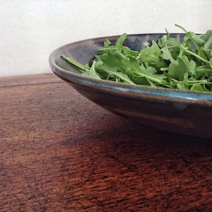 May include: A dark blue ceramic bowl filled with fresh green arugula.