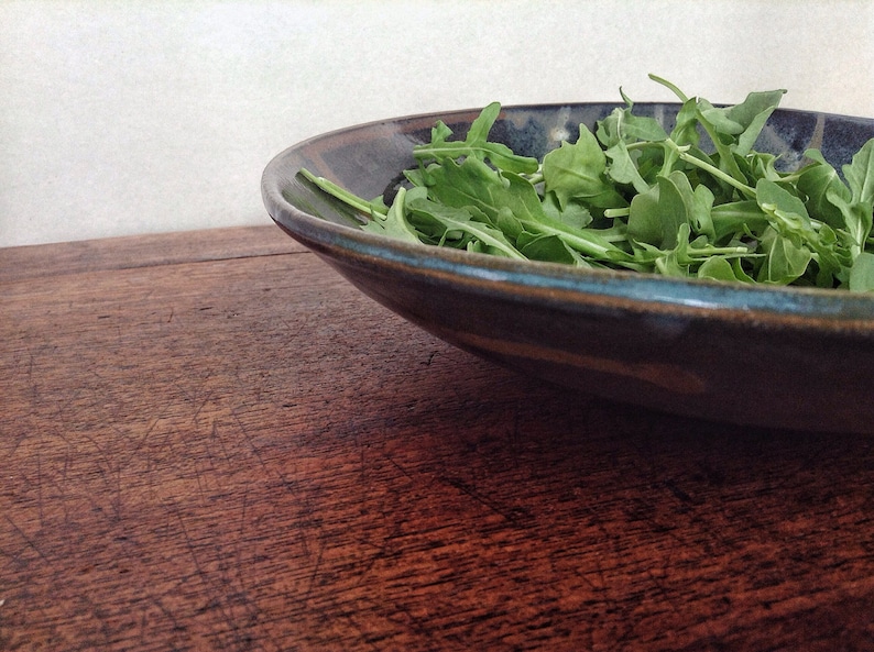May include: A dark blue ceramic bowl filled with fresh green arugula.