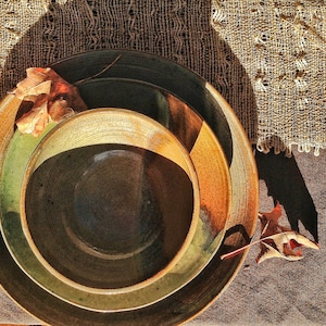 May include: Two ceramic bowls, one nested inside the other. The larger bowl is brown with green and brown streaks. The smaller bowl is dark brown with a smooth, glossy finish. Both bowls have a rustic, handmade look.