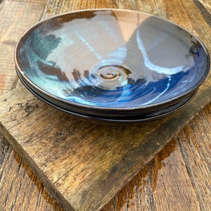 May include: Two ceramic bowls with a blue and brown glaze. The bowls are stacked on top of each other and are sitting on a wooden surface.