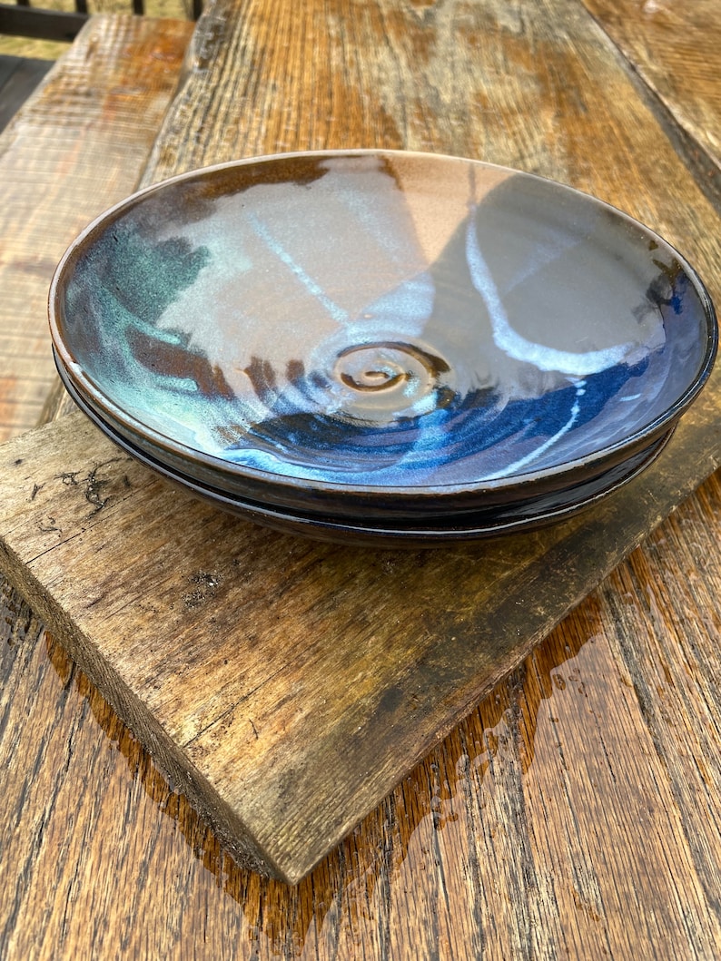 May include: Two ceramic bowls with a blue and brown glaze. The bowls are stacked on top of each other and are sitting on a wooden surface.