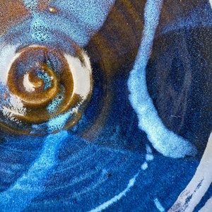 May include: A close-up of a ceramic bowl with a blue and brown glaze. The bowl has a swirl pattern in the center and a white line running along the edge.