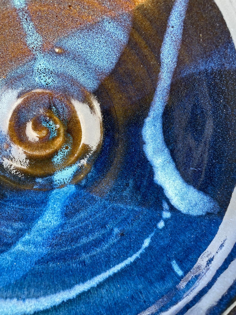 May include: A close-up of a ceramic bowl with a blue and brown glaze. The bowl has a swirl pattern in the center and a white line running along the edge.