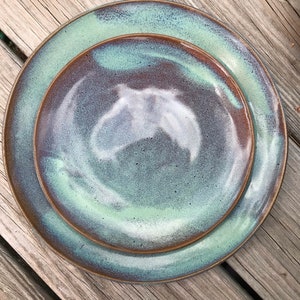 May include: A set of two ceramic plates with a green and brown glaze. The plates have a swirling pattern and a speckled finish.