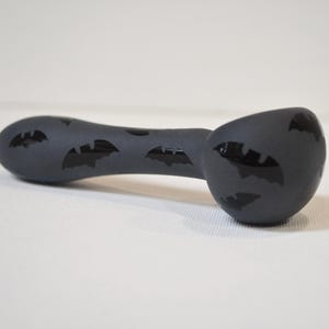 May include: A dark gray pipe with black bat silhouettes. The pipe has a rounded bowl and a curved stem. The bat symbols are evenly spaced across the surface of the pipe.