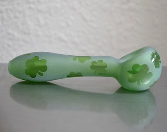 May include: A frosted green glass pipe with a shamrock design. The pipe is on a white surface.