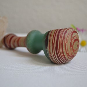 May include: A green and red glass pipe with a swirl pattern. The pipe is made of glass and has a round bowl.