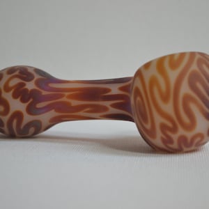 May include: A glass pipe with a brown and white swirl pattern. The pipe is made of glass and has a rounded bowl and a long, thin stem.