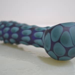 Op de afbeelding: Een blauwe en paarse glazen pijp met een draaiend patroon. De pijp is gevormd als een lange, dunne buis met een afgeronde kom aan het ene uiteinde.
