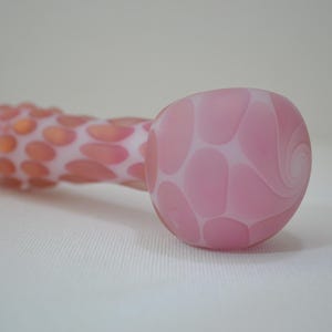 May include: A pink glass pipe with a swirl design and a textured, spotted body.