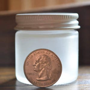 May include: A frosted glass jar with a white lid. The jar is about the size of a US quarter.