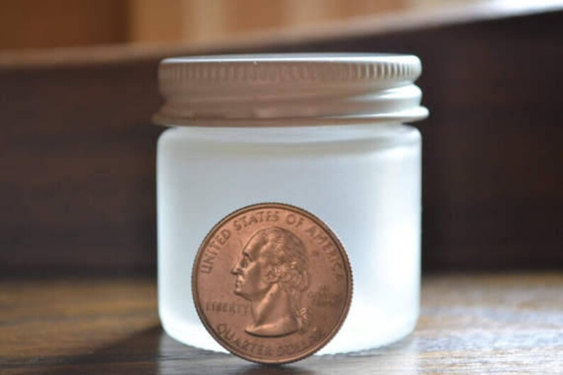 May include: A frosted glass jar with a white lid. The jar is about the size of a US quarter.