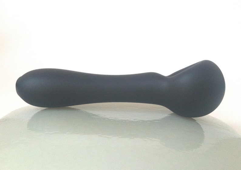 May include: A dark gray glass pipe with a rounded bowl and a long, curved stem.