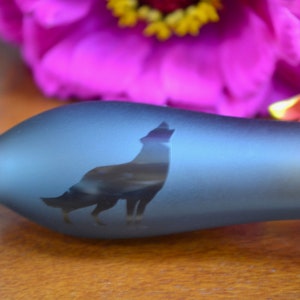 May include: A blue glass bottle with a wolf silhouette etched into the side. The bottle is frosted and has a smooth, rounded shape.