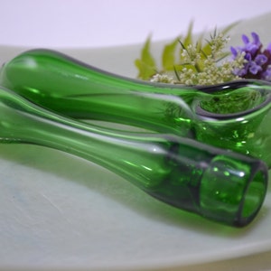 May include: Two green glass pipes, one with a bowl, on a white surface. The pipes have a clear, almost white, swirl design.