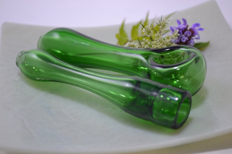 May include: Two green glass pipes, one with a bowl, on a white surface. The pipes have a clear, almost white, swirl design.