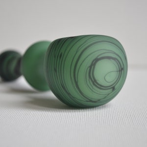May include: Three green glass vases with black swirl designs. The vases are different sizes and are arranged in a row.