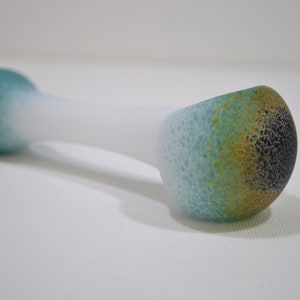 May include: A glass pipe with a white body and blue, green, and gold accents. The pipe has a rounded bowl and a long, thin stem.
