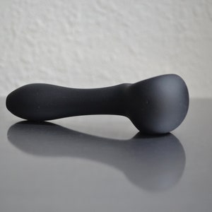May include: A black, smooth, curved object with a rounded end. The object is lying on a gray surface.