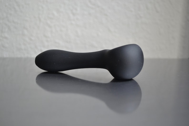 May include: A black, smooth, curved object with a rounded end. The object is lying on a gray surface.