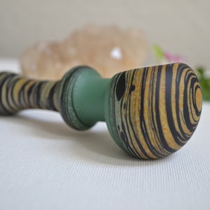 May include: A wooden smoking pipe with a green and black swirl design. The bowl of the pipe is round and has a black and yellow swirl design.