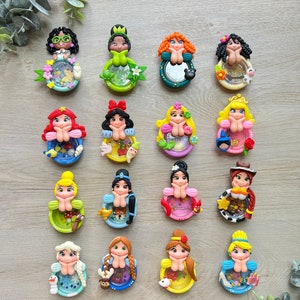 May include: A set of 16 colorful resin charms featuring Disney princesses. Each charm is a round, clear resin dome with a miniature princess figurine inside. The princesses are all in different poses and outfits, and each charm has a different background and glitter.