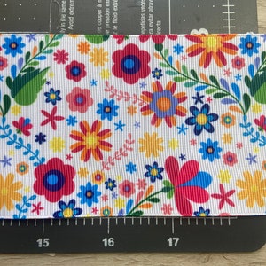 Puede incluir: Cinta blanca con un patr&oacute;n floral colorido. El patr&oacute;n presenta flores rojas, rosas, amarillas, azules y verdes sobre un fondo blanco.