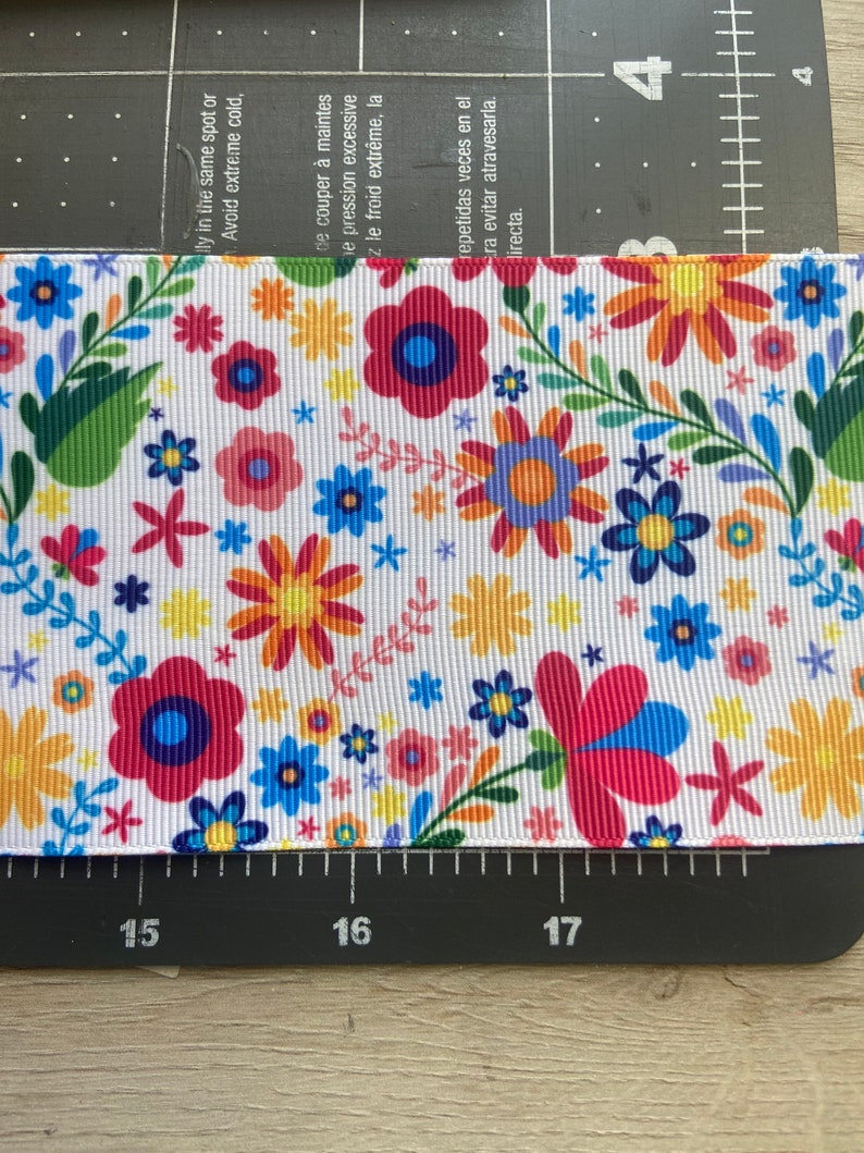 Puede incluir: Cinta blanca con un patr&oacute;n floral colorido. El patr&oacute;n presenta flores rojas, rosas, amarillas, azules y verdes sobre un fondo blanco.