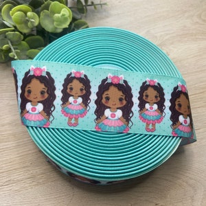 May include: A roll of turquoise ribbon with a repeating pattern of cartoon girls in dresses. The ribbon is approximately 1 inch wide and is suitable for crafts, gift wrapping, or hair accessories.