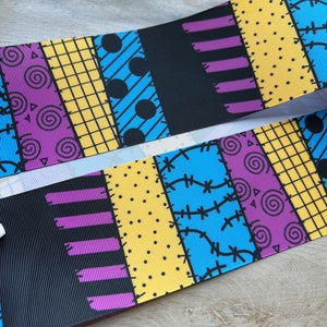 May include: Two ribbons with a patchwork design in blue, yellow, purple, and black. The design includes spirals, dots, and stitched patterns. The ribbons are likely for crafting or decorative purposes.