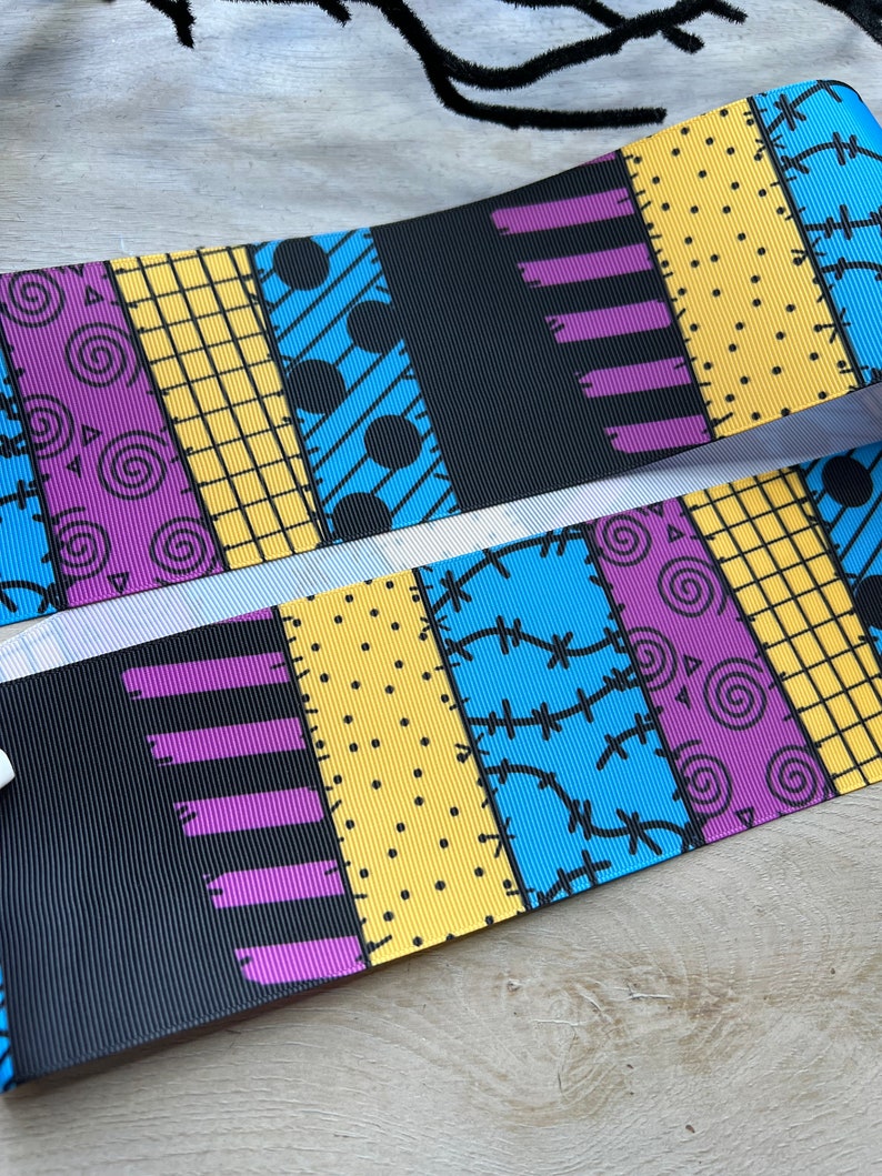 May include: Two ribbons with a patchwork design in blue, yellow, purple, and black. The design includes spirals, dots, and stitched patterns. The ribbons are likely for crafting or decorative purposes.