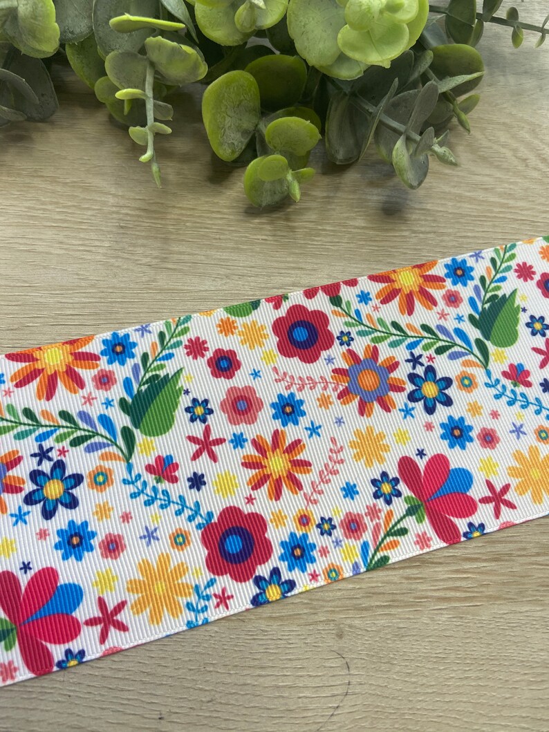 Puede incluir: Cinta blanca con un patr&oacute;n floral colorido. El patr&oacute;n presenta flores rojas, amarillas, azules, verdes y rosas sobre un fondo blanco.