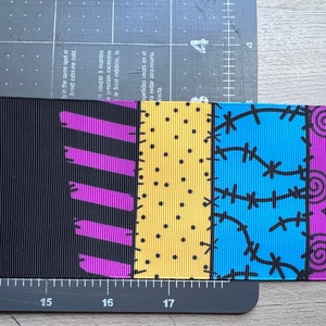 May include: Ribbon with a patchwork design featuring various patterns and colors. The ribbon includes black, purple, yellow, and blue sections with polka dots, stitches, and swirls. The ribbon is approximately 2 inches wide.