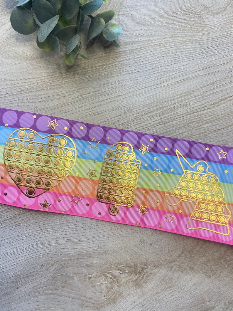 Pu&ograve; includere: Un nastro a righe arcobaleno con accenti dorati. Il nastro presenta un cuore, un ghiacciolo e un unicorno con un design pop-it.
