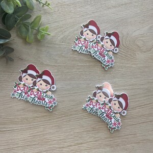 May include: Several Christmas-themed stickers featuring cartoon characters wearing red and white Santa hats. Each sticker has the text "Cold Days Warm Hearts" with holly and snowflake accents. The stickers are on a light wood surface.
