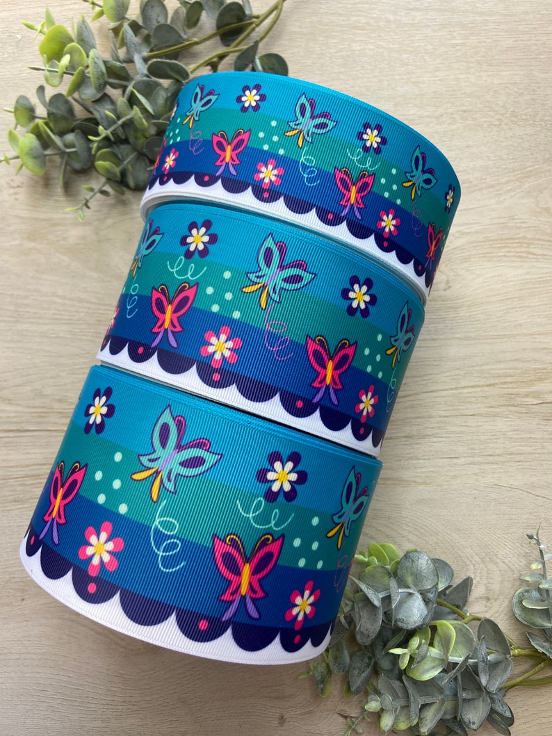 Pu&ograve; includere: Tre rotoli di nastro blu con un bordo bianco a festoni. Il nastro ha un motivo colorato di farfalle e fiori.