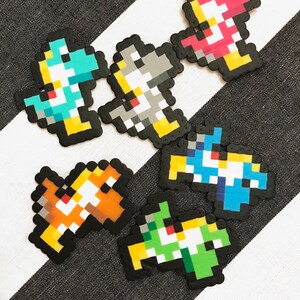 May include: A collection of pixel art figures in various colors, including teal, gray, pink, orange, blue, and green. Each figure has a black outline and is arranged on a black and white striped surface.
