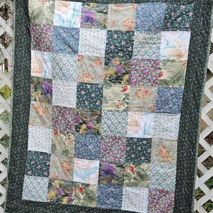 May include: A patchwork quilt with a green border and a variety of floral patterns in shades of green, pink, purple, and white.
