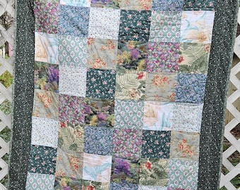 Può includere: Una trapunta patchwork con un bordo verde e una varietà di motivi floreali in tonalità di verde, rosa, viola e bianco.