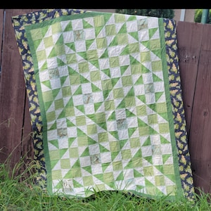 Puede incluir: Una colcha verde y blanca con un patrón geométrico. La colcha tiene un borde negro y verde con un diseño de vid.