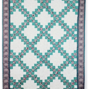 May include: A white quilt with a teal and pink floral pattern. The quilt is made up of squares arranged in a grid pattern. The quilt has a teal and pink border.