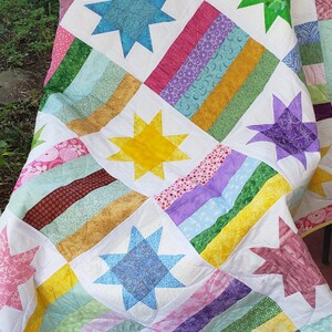 May include: A colorful patchwork quilt with a white background and a variety of star-shaped patterns in shades of blue, green, yellow, purple, and pink.