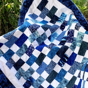 May include: A blue and white patchwork quilt with a quilted pattern of circles. The quilt is made of various shades of blue fabric with a white background.