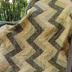 May include: A green and beige quilt with a geometric pattern. The quilt is folded and has a dark green border.