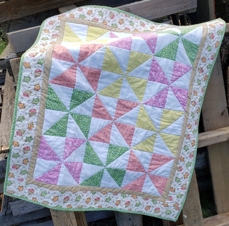 May include: A handmade quilt with a pinwheel pattern in shades of pink, green, yellow, and white. The quilt has a border with a brown and white birdhouse print.