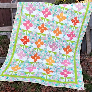 May include: A colorful quilt with a floral pattern. The quilt features a repeating design of pink, orange, and green flowers on a white background. The quilt is bordered with a green and yellow trim.