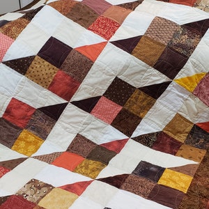 May include: A quilt with a patchwork design featuring a variety of brown, orange, and yellow fabrics. The quilt is made up of squares and triangles, and the fabric patterns are floral, geometric, and abstract.
